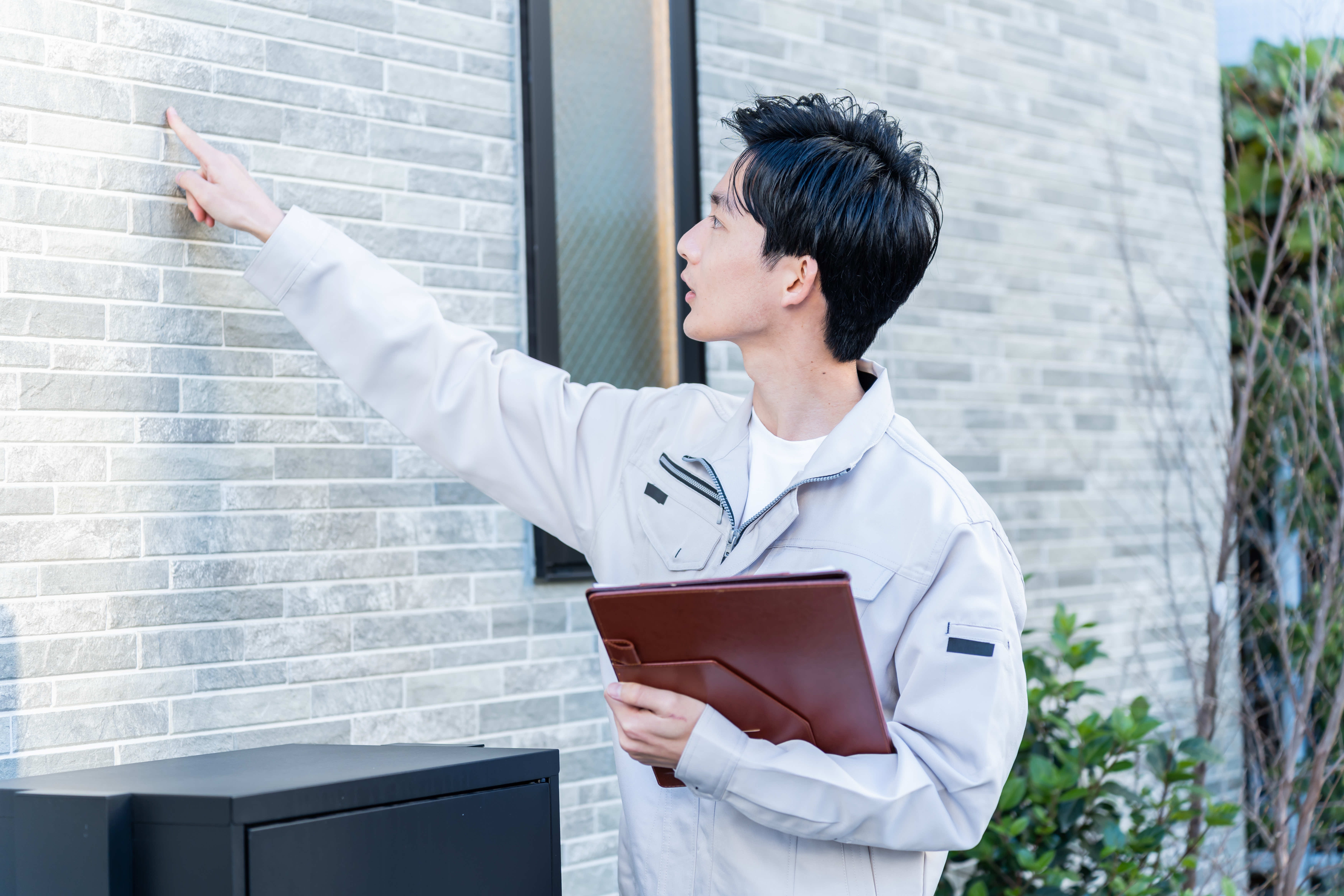 作業服を着た男性が、建物の外壁を指差しながら確認している様子