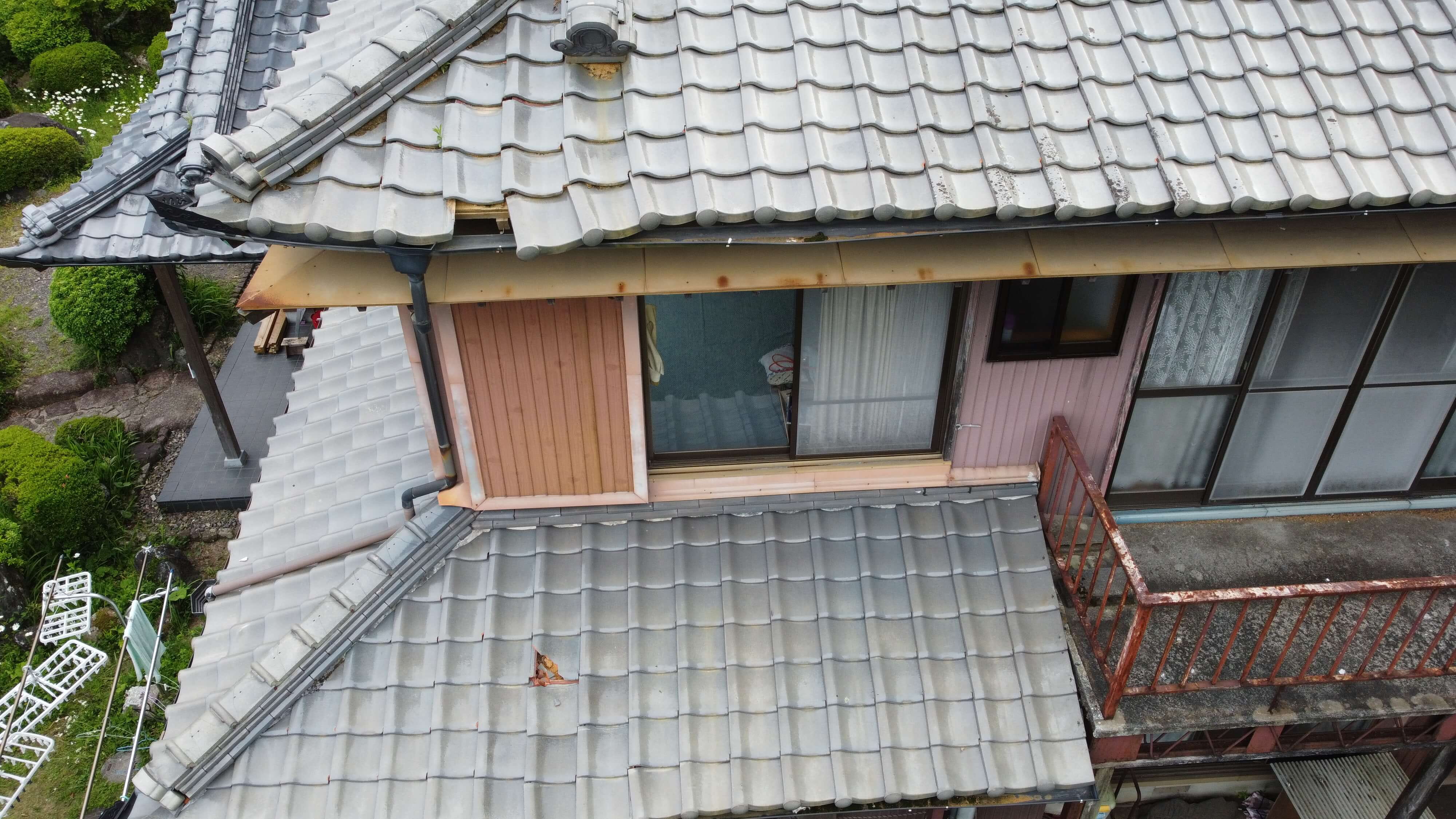 古い瓦屋根の住宅で、サビが見られる金属製の庇と木造の外壁が特徴的な建物